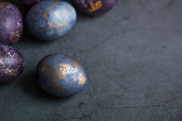 Easter card with a copy of the place for the text. Purple, blue and golden eggs on a dark background. The trend of 2022 purple shade is very peri. Natural dye karkade tea. Top view.