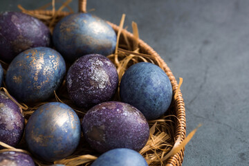 Easter card with a copy of the place for the text. Purple, blue and golden eggs in a basket on a dark background. The purple hue trend of 2022 is very peri. Natural dye karkade tea. Top view.
