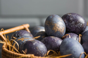 Easter card with a copy of the place for the text. Purple, blue and golden eggs in a basket on a dark background. The purple hue trend of 2022 is very peri. Natural dye karkade tea. Top view.