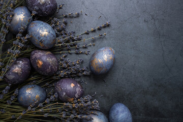 Easter card with a copy of the place for the text. Purple, blue and golden eggs with lavender on a dark background. The purple hue trend of 2022 is very relevant. Natural dye karkade tea. Top view.
