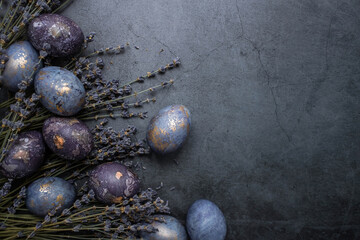 Easter card with a copy of the place for the text. Purple, blue and golden eggs with lavender on a dark background. The purple hue trend of 2022 is very relevant. Natural dye karkade tea. Top view.