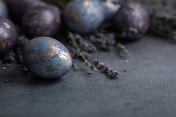 Easter card with a copy of the place for the text. Purple, blue and golden eggs with lavender on a dark background. The purple hue trend of 2022 is very relevant. Natural dye karkade tea. Top view.