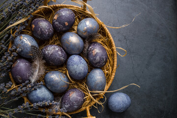 Easter card with a copy of the place for the text. Purple, blue and golden eggs with lavender on a dark background. The purple hue trend of 2022 is very relevant. Natural dye karkade tea. Top view.