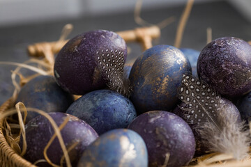 Easter card with a copy of the place for the text. Purple, blue and golden eggs in a basket on a dark background. The purple hue trend of 2022 is very peri. Natural dye karkade tea. Top view.