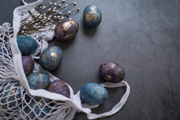 Easter card with a copy of the place for the text. Purple, blue and golden eggs in a string bag on a dark background. The trend of 2022 purple shade is very peri. Natural dye karkade tea. Top view.