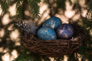 Happy Easter 2022. A postcard with a copy of the place for the text. Purple, blue and golden eggs in a nest on a natural forest background. Top view.