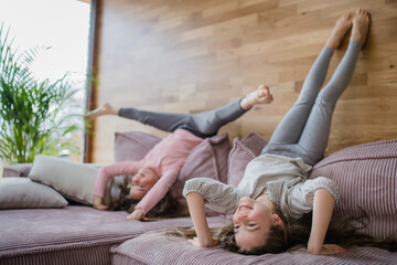 Happy little sisters doing head stand on sofa at home.