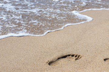 Footprints of a man on the yellow beach sand from walking barefoot by the sea with water that washes away the footprints.
