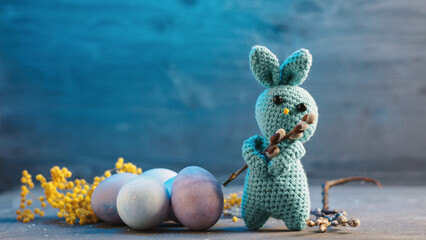 Easter banner, knitted Easter bunny with willow branch and pastel colored eggs on a blue background copy space