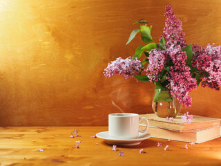 A cup of hot coffee or tea on a wooden table and a vase with a bouquet of lilac. Copy space