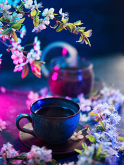 Stylish spring composition with a cup of coffee and blooming branches of white cherry. Neon light. Spring holiday card