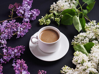 Obraz na płótnie Canvas a white cup of coffee on a black table and lilac branches