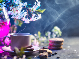 spring still life with a cup of hot coffee and branches of white cherry. oatmeal cookies and chocolate. neon backlight