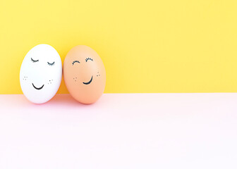 Easter concept. Two creative white and brown eggs with painted eyes and a mouth on a yellow-pink background. Free place.