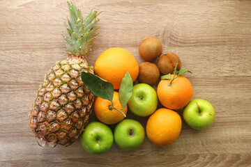 Pineapple, apples, oranges, lemons and kiwis on a wooden table. Top view.