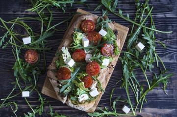 Fresh pinsa with cheese, tomatoes, cabbage and arugula on a natural wooden background top view.