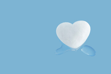 Heart-shaped melting snowball and drops of water on isolated pastel blue background. Concept of...