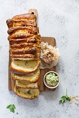 Homemade fresh  pull apart bread with herbs (parsley, thyme, rosemary, dill), garlic, cheese and spicy butter on a wooden board.