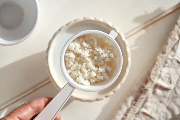 Fresh kefir grains in a white sieve over a bowl of milk
