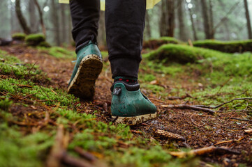 Close photo of a tourist's feet in boots walking on wet ground with moss in the woods during a hike in the woods