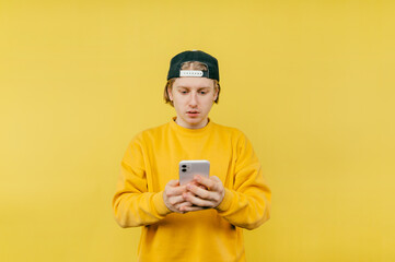 Handsome guy in a cap uses a smartphone with a serious face on a yellow background. Isolated