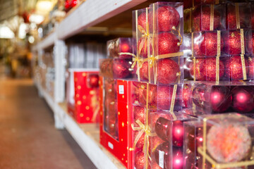 Closeup of packaging boxes with red shiny Christmas baubles on supermarket shelves. Concept of traditional holiday decorations