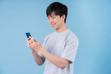 Young Asian man using smartphone on blue background