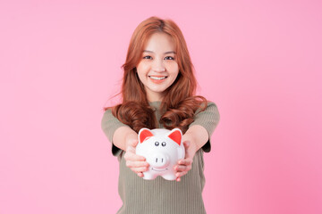 Fototapeta na wymiar Young Asian woman holding piggy bank on pink background