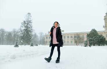 Funny lady stands on the street of the town in a blizzard and having fun with a happy face on a background of winter snowy landscape, full-length photo.