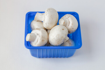 Fresh mushrooms champignons in a plastic blue tray. Close up mushrooms champignons in the blue...