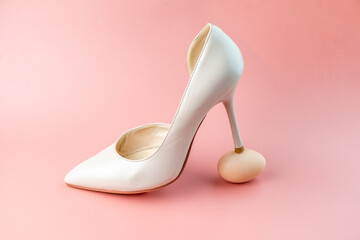 A woman's white shoe stands with a heel on a chicken egg. Concept photo.