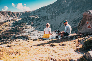 Fototapeta premium couple with dog sitting on rocks admiring mountain landscape slow travel
