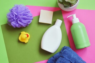 White shampoo bottle, green liquid soap package, purple sponge and rubber duck view from above image. Flat lay composition photography bath products, kids cosmetics
