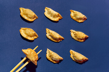 Pattern of fried gyoza dumplings, chopsticks holding one of them against a blue background