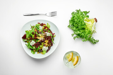 Salad with beets, feta cheese and lettuce in a composition with greens and a glass of water on a white background. Top view
