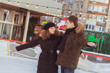 A young couple in love skating on a skating rink, arms apart, look at each other and smile