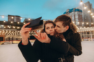 A young couple in love hugs and takes a selfie on an ice rink