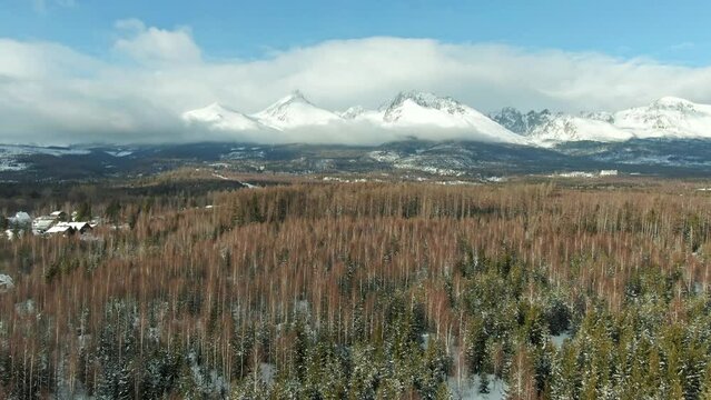 Aerial drone view of High Tatras mountains panorama, Slovakia. Mountain peaks covered with snow in winter. Forest and wild nature, blue sky with clouds. Vysoke Tatry in local speak.