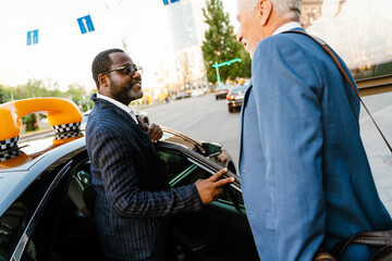 Multiracial men smiling and handshaking while standing by taxi