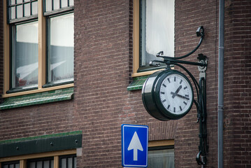 Obraz premium The street clock on the brick façade and arrow traffic sign, Leiden Netherlands