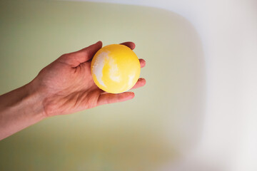 Woman's hand putting yellow bath bomb into water top view. Melon banana scented bomb with sea salt in hand against backdrop of bathtub full of water. Spa and relax at home. Copy space, place for text.
