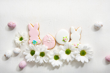 Overhead view of  Easter bunny and eggs cookies and white flowers on light surface spring holiday