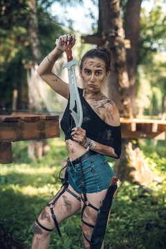 beautiful young girl in short shorts and a T-shirt smeared with swamp holds a dagger
