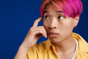 Asian boy with pink hair rubbing his temple and looking aside