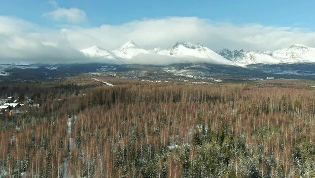 Aerial drone view of High Tatras mountains panorama, Slovakia. Mountain peaks covered with snow in winter. Forest and wild nature, blue sky with clouds. Vysoke Tatry in local speak.