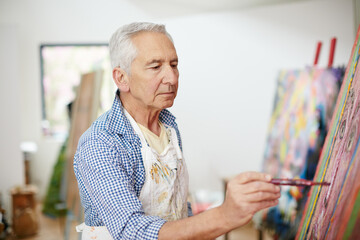The creative adult is the child who survived. Shot of a senior man working on a painting at home.