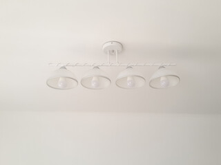 Chandelier lamp for four energy-saving lamps on a white ceiling with a bright room.