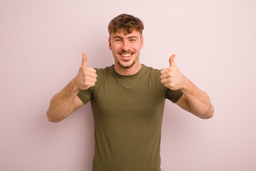 young cool man smiling broadly looking happy, positive, confident and successful, with both thumbs...