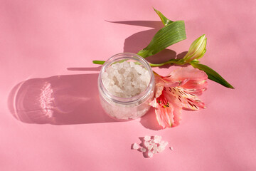 White bath salt with flowers on a pink background. Perfumed salt in a bottle. 
