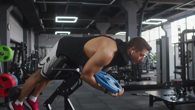 Man athletic build trains muscles of abs in gym lifting weight plates, side view. Man workout in gym trains muscles of abs